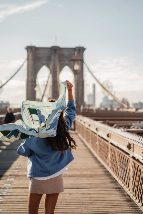 Une femme marche sur le pont de New York avec un foulard au vent dans sa main