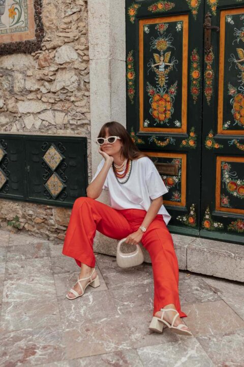 tenue femme t-shirt blanc et pantalon rouge avec sandales blanches, lunettes de soleil et sac nacré